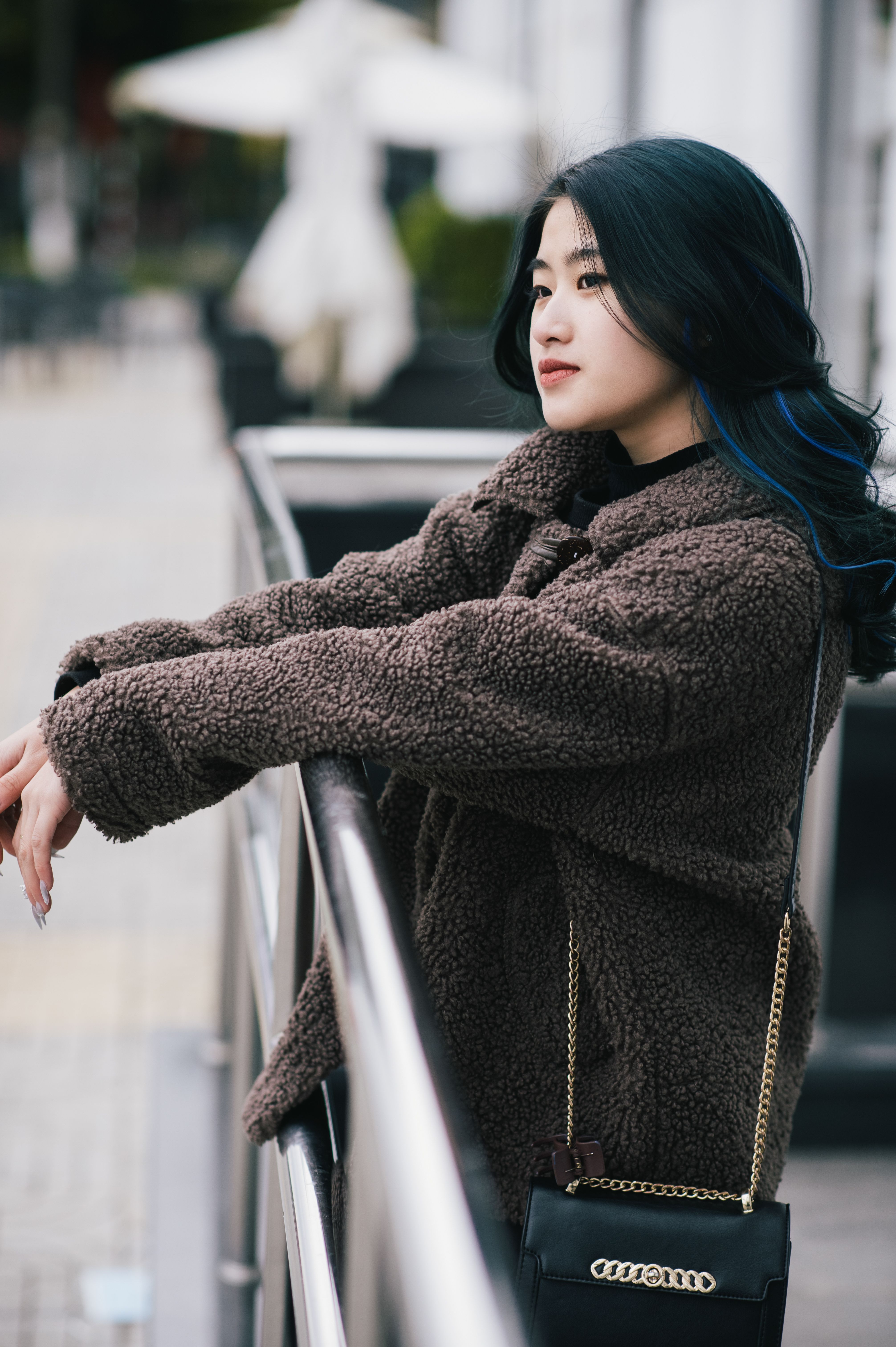 Asian woman in fashionable outfit leaning on railing in urban setting.