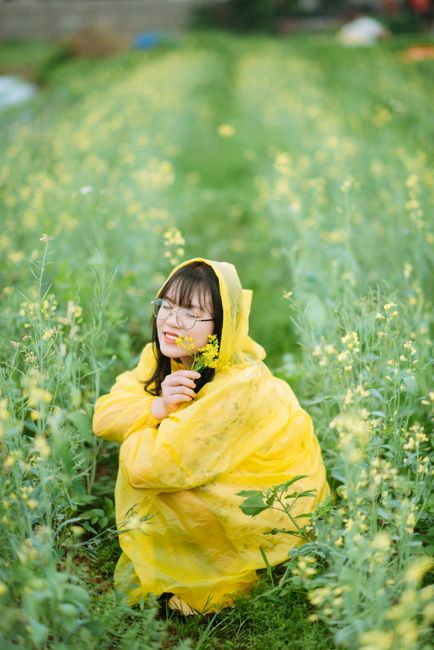 A young woman in a yellow raincoat enjoys the outdoors, surrounded by a blooming flower field.