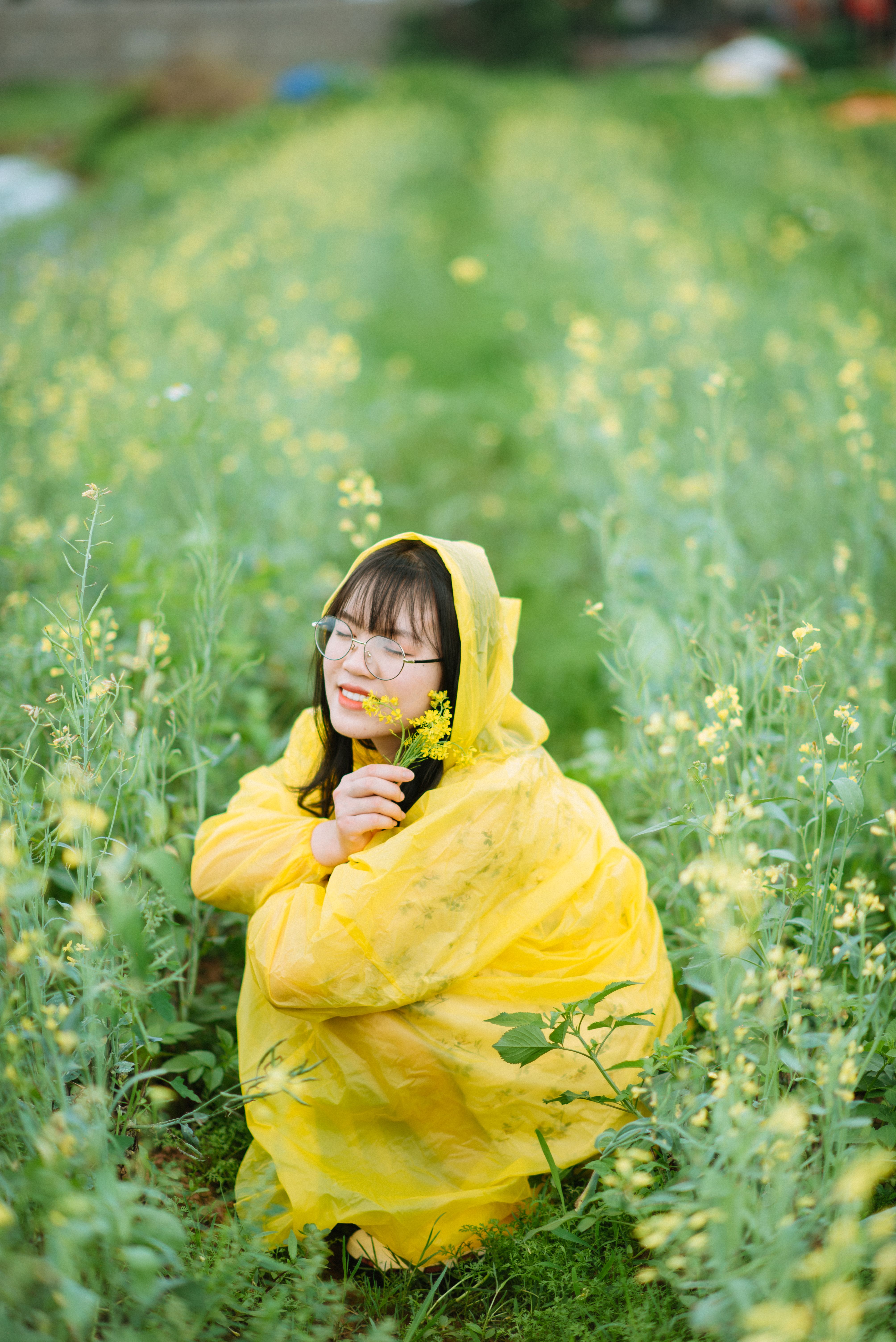 Young Woman in a Yellow Raincoat Crouching on a Field · Free Stock Photo