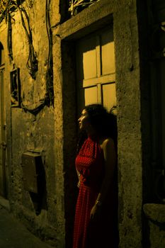 A woman in a red dress poses against an old building in dimly lit Istanbul street.
