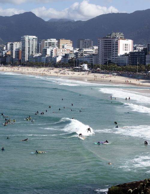 Free A lively beach in Rio de Janeiro showcasing surfers and coastal cityscape with mountains. Stock Photo