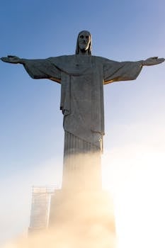 Iconic Christ the Redeemer statue in Rio de Janeiro, Brazil at sunrise, emerging from mist.