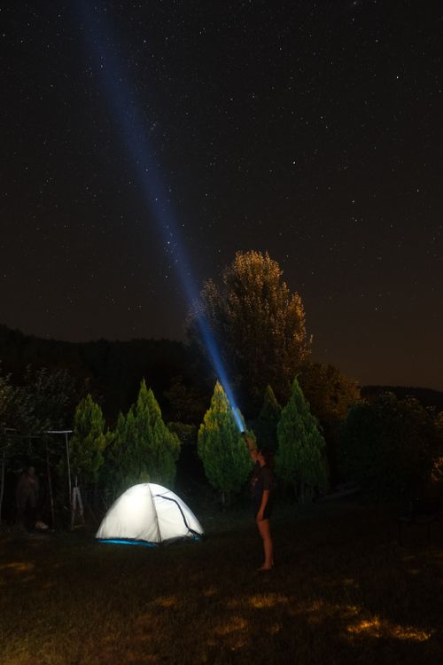 Free A person using a flashlight near a tent under a starry night sky, surrounded by trees. Stock Photo