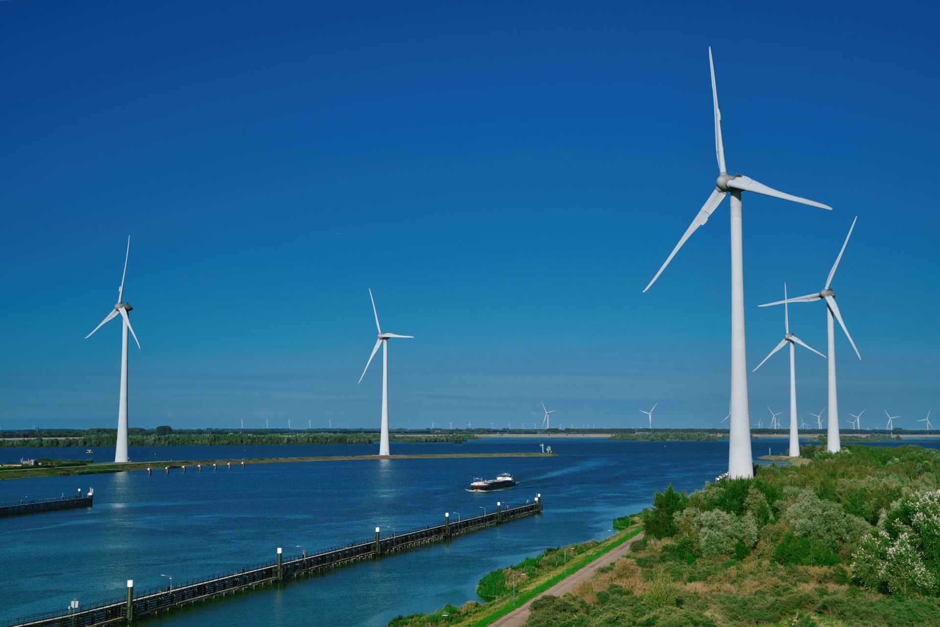 Renewable wind energy turbines standing over water under a clear blue sky in Bruinisse.