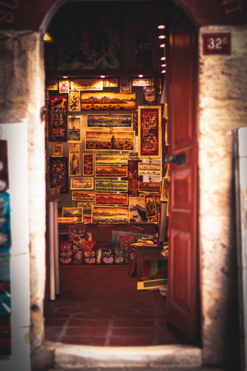 Free Cozy art shop entrance showcasing an array of paintings and artworks through an open door. Stock Photo