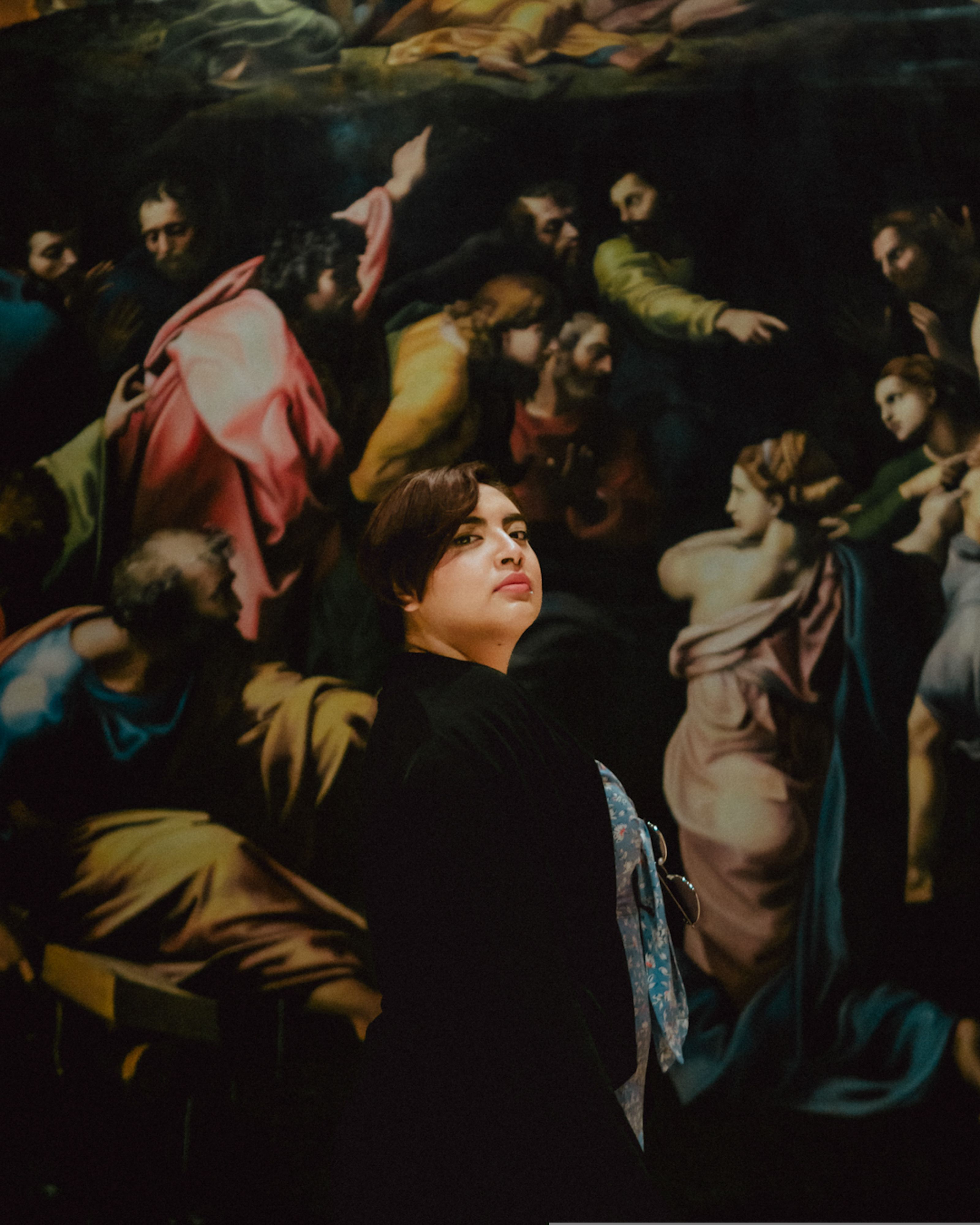 A woman stands before a vibrant Renaissance painting in a museum setting.