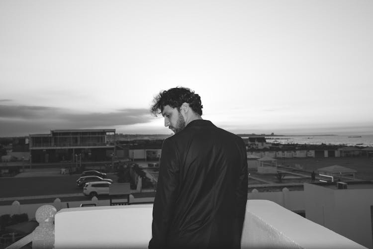 Black And White Photo Of Man Standing On Rooftop Overlooking City