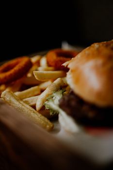 Close-up of a tasty burger served with fries and crispy onion rings.