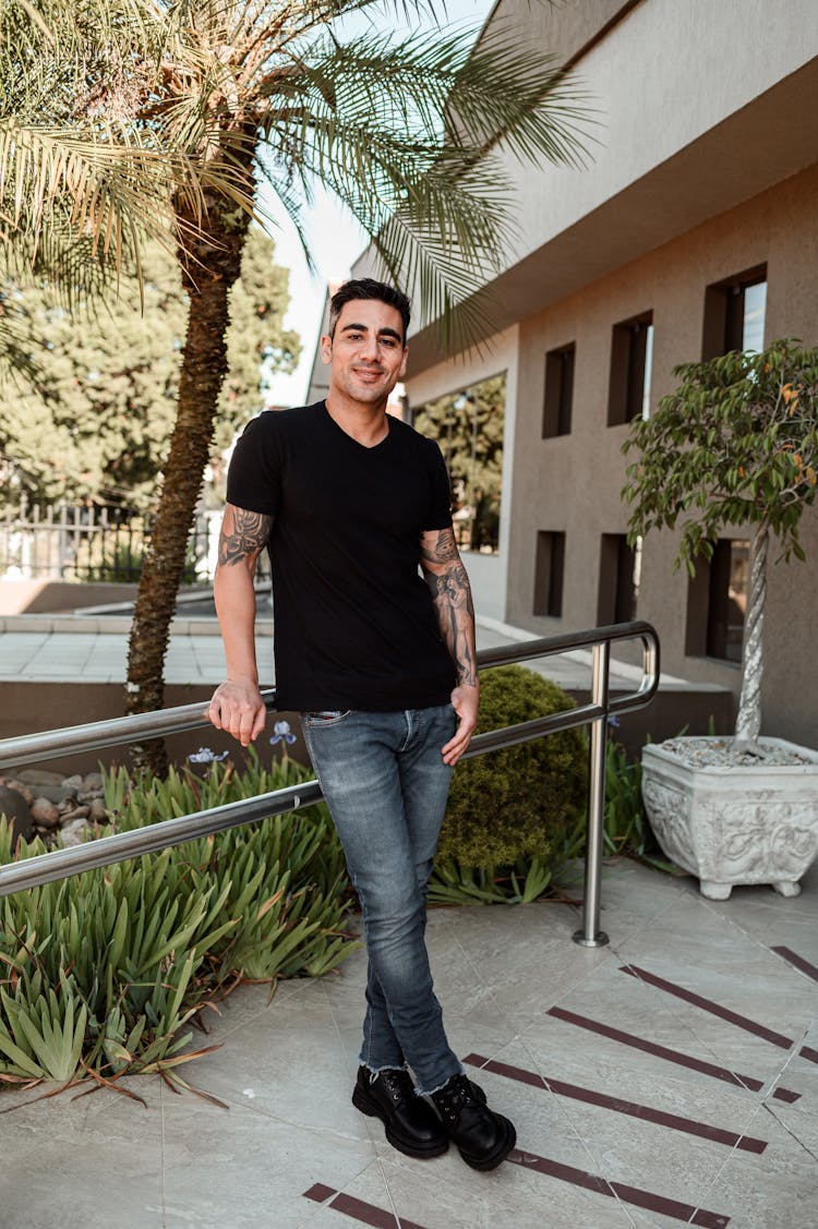 Man Standing In Front Of House Entrance Next To Palm Trees