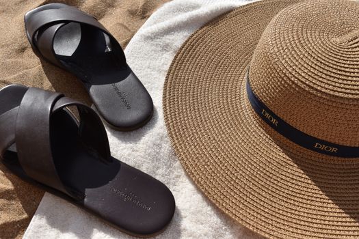 Close-up of a sun hat, sandals, and towel on sandy beach, perfect for summer vibes.