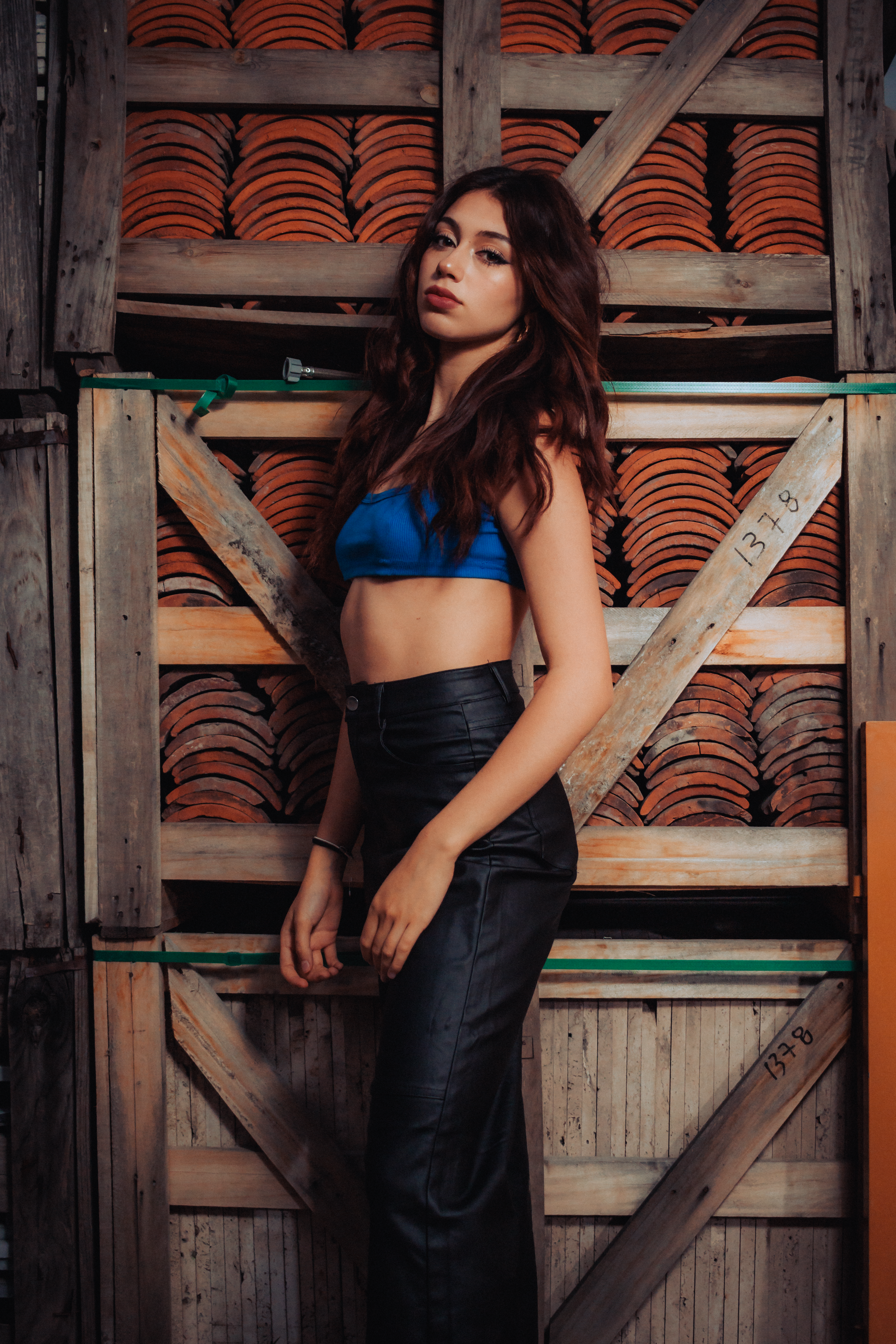 Young woman posing stylishly in black trousers and a blue crop top, construction backdrop.