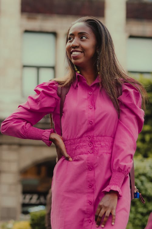 Young Smiling Woman in a Pink Dress Standing Outside 