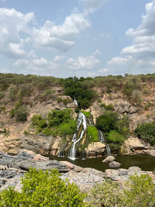 Free Beautiful cascading waterfall amidst rocky terrain and lush greenery under a cloudy sky. Stock Photo
