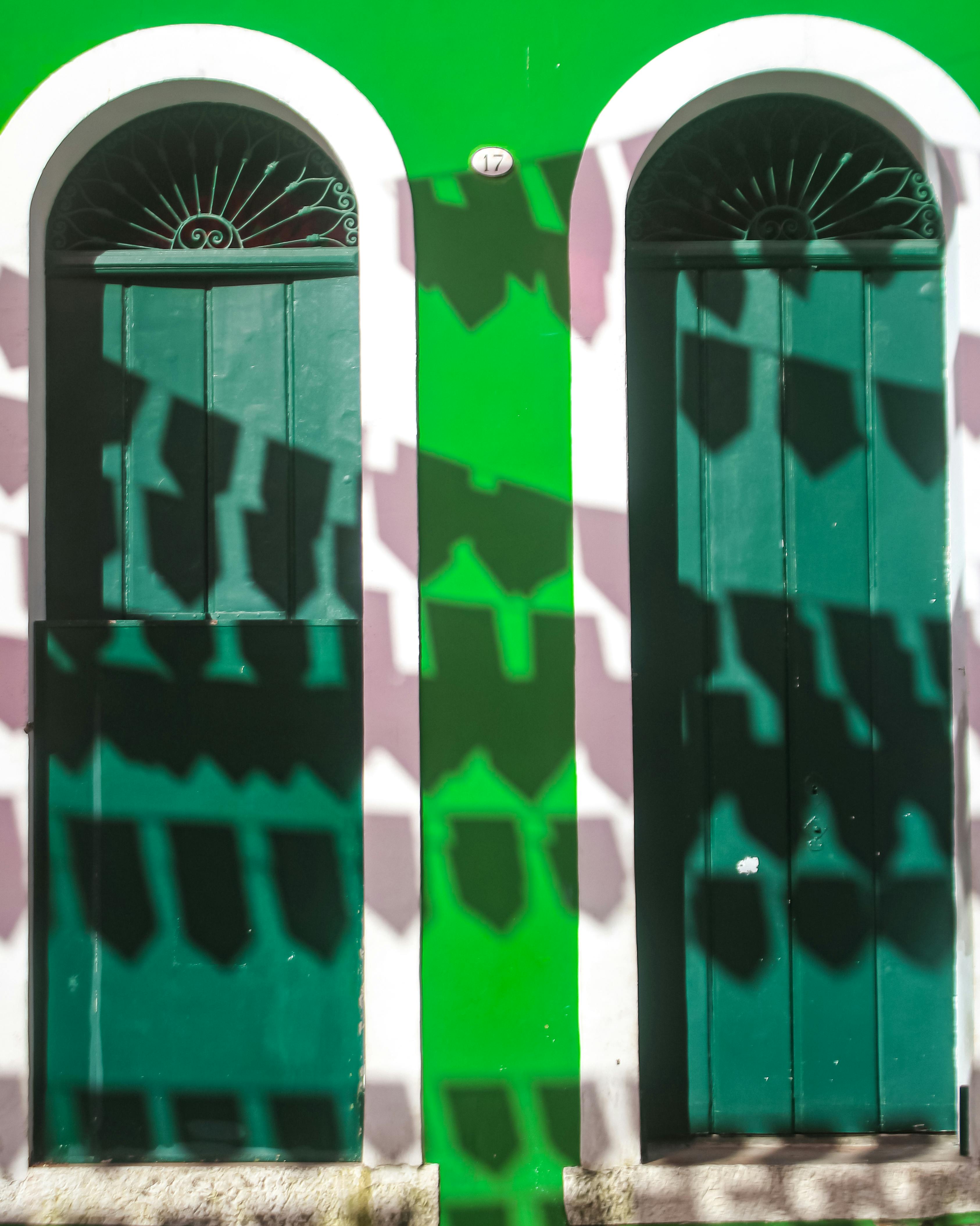 Two green arched doors with dynamic shadows on a colorful facade.