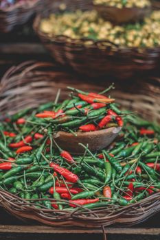 Fresh red and green chili peppers displayed in woven baskets at a market stall.