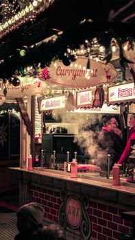 A cozy and vibrant night scene at a festive street food market, showcasing a currywurst stall.