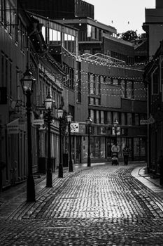 A deserted cobblestone city street with string lights overhead, captured in black and white.