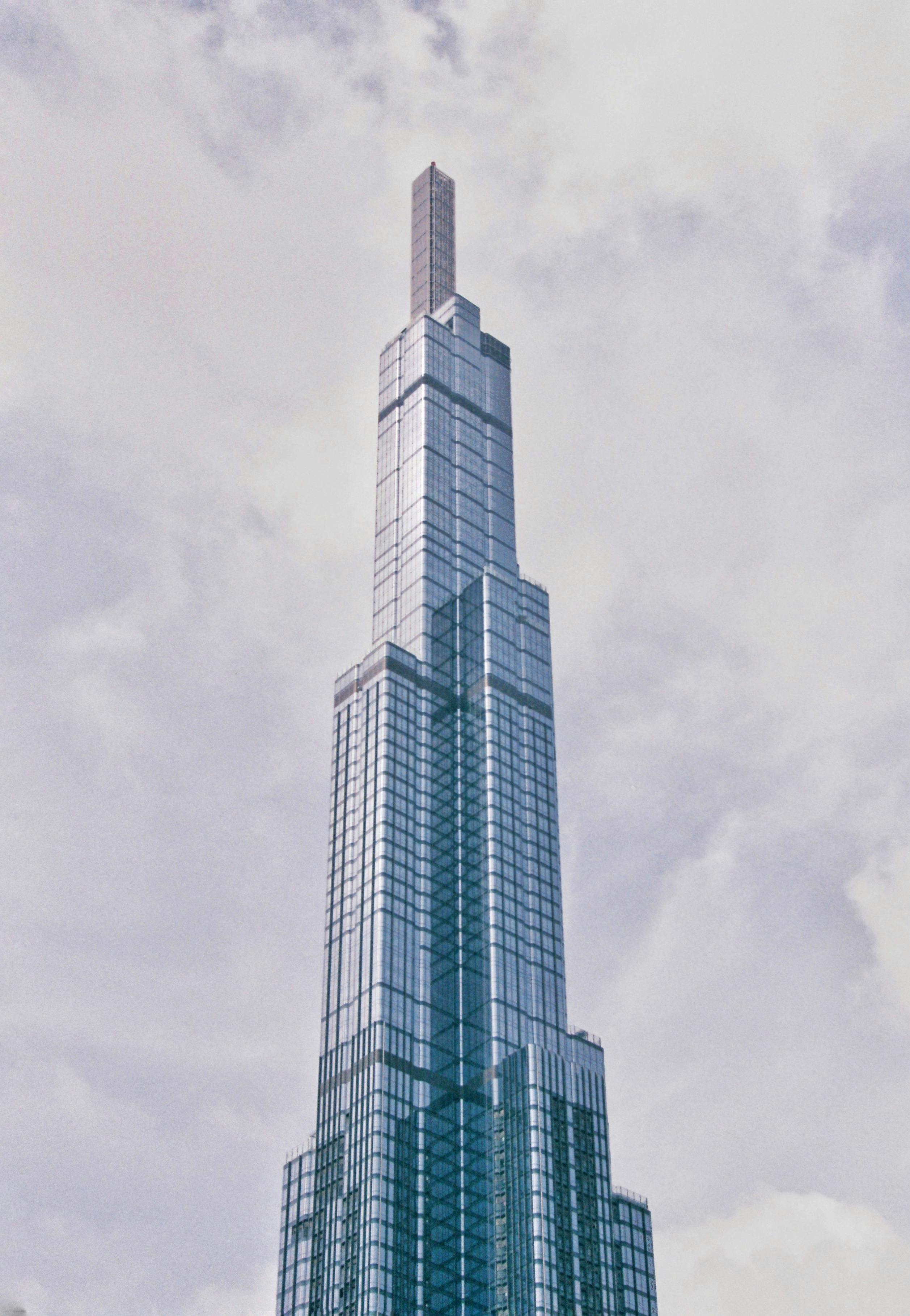 A towering modern glass skyscraper reaching towards the cloudy sky.