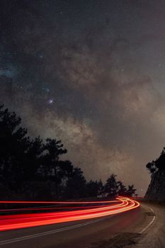 Dramatic light trails on a curved road beneath a star-studded night sky in Karaisalı, Türkiye.