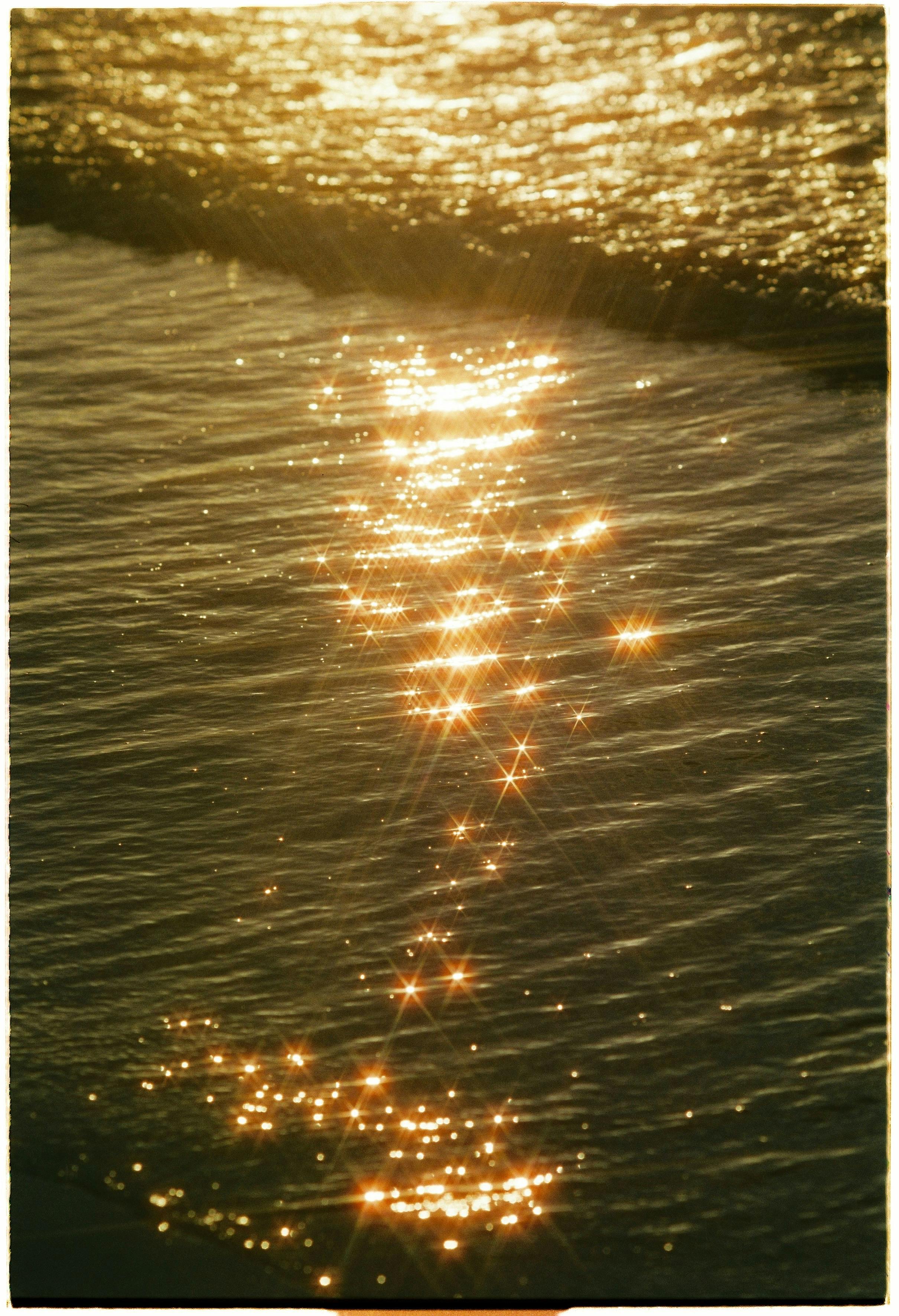 Sparkling golden sunlight creates a mesmerizing pattern on the ocean surface during sunset.