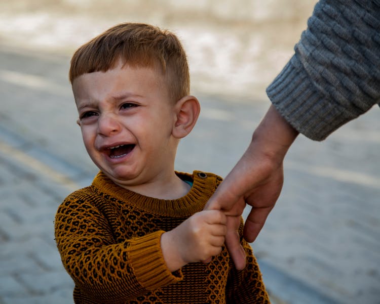 A Little Boy Holding His Parent Hand And Crying 