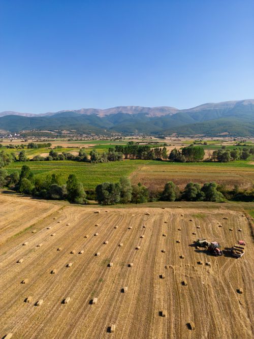 Free Aerial view of harvested fields with hay bales and a tractor under a clear blue sky. Stock Photo