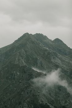 A moody mountain peak surrounded by clouds, showcasing rugged rocky terrain and a dramatic atmosphere.