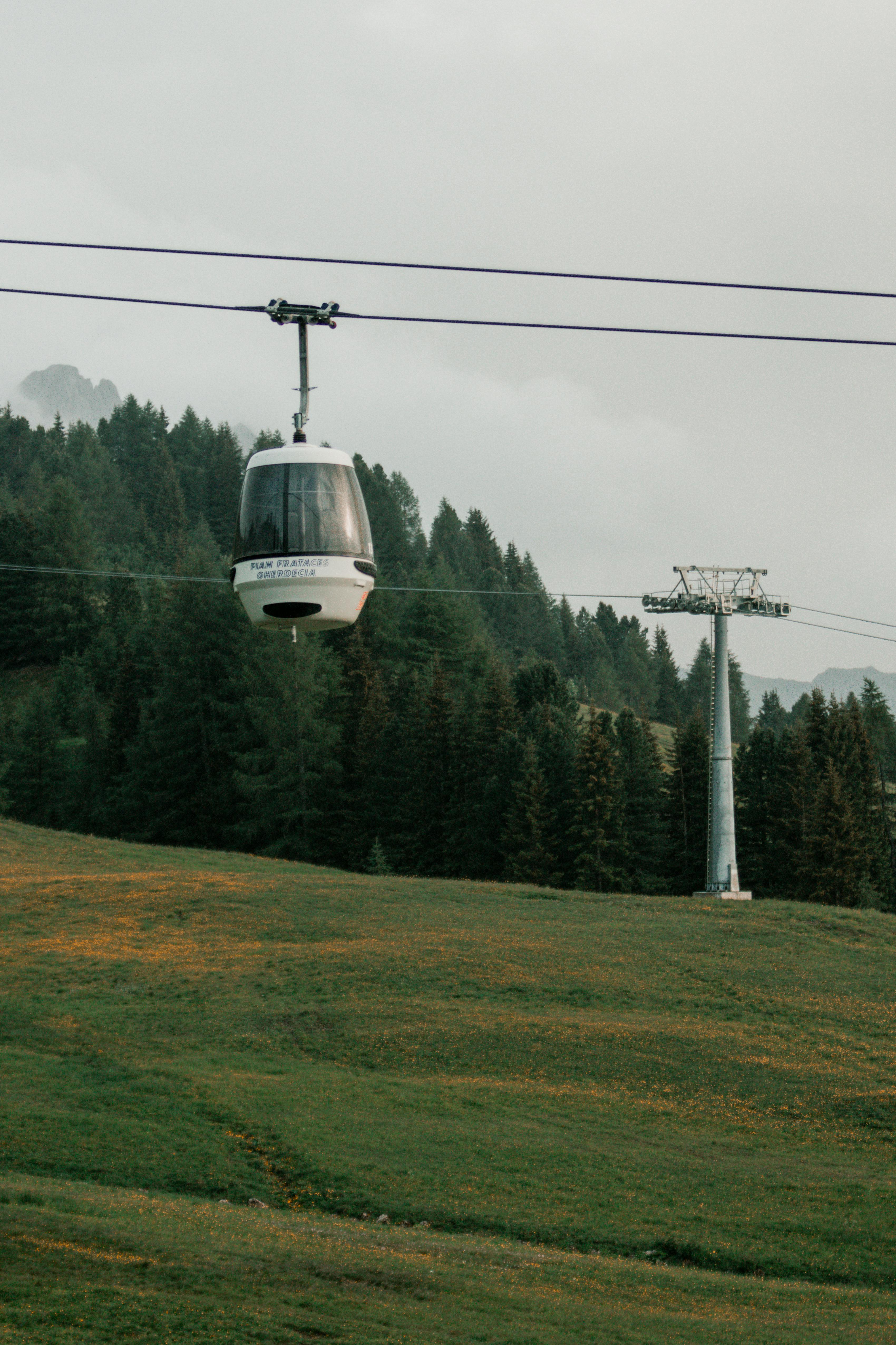 Gondola lift traveling over lush mountain forest during summer day, offering scenic views.