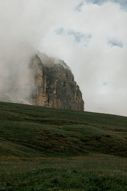 Free Landscape of a Green Hill and a Rocky Mountain in Clouds  Stock Photo