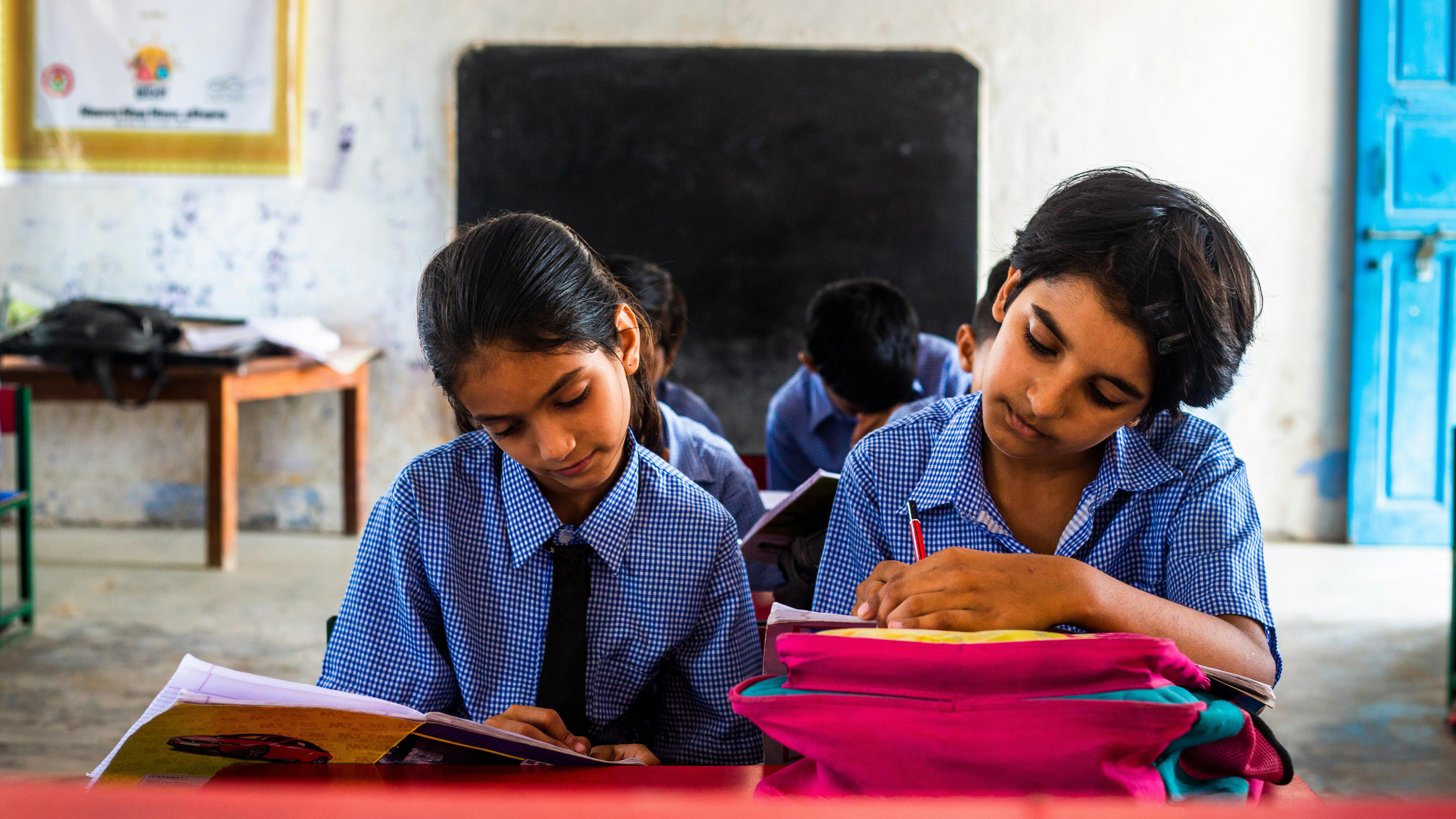 Two Indian children in school uniforms concentrating on their studies.