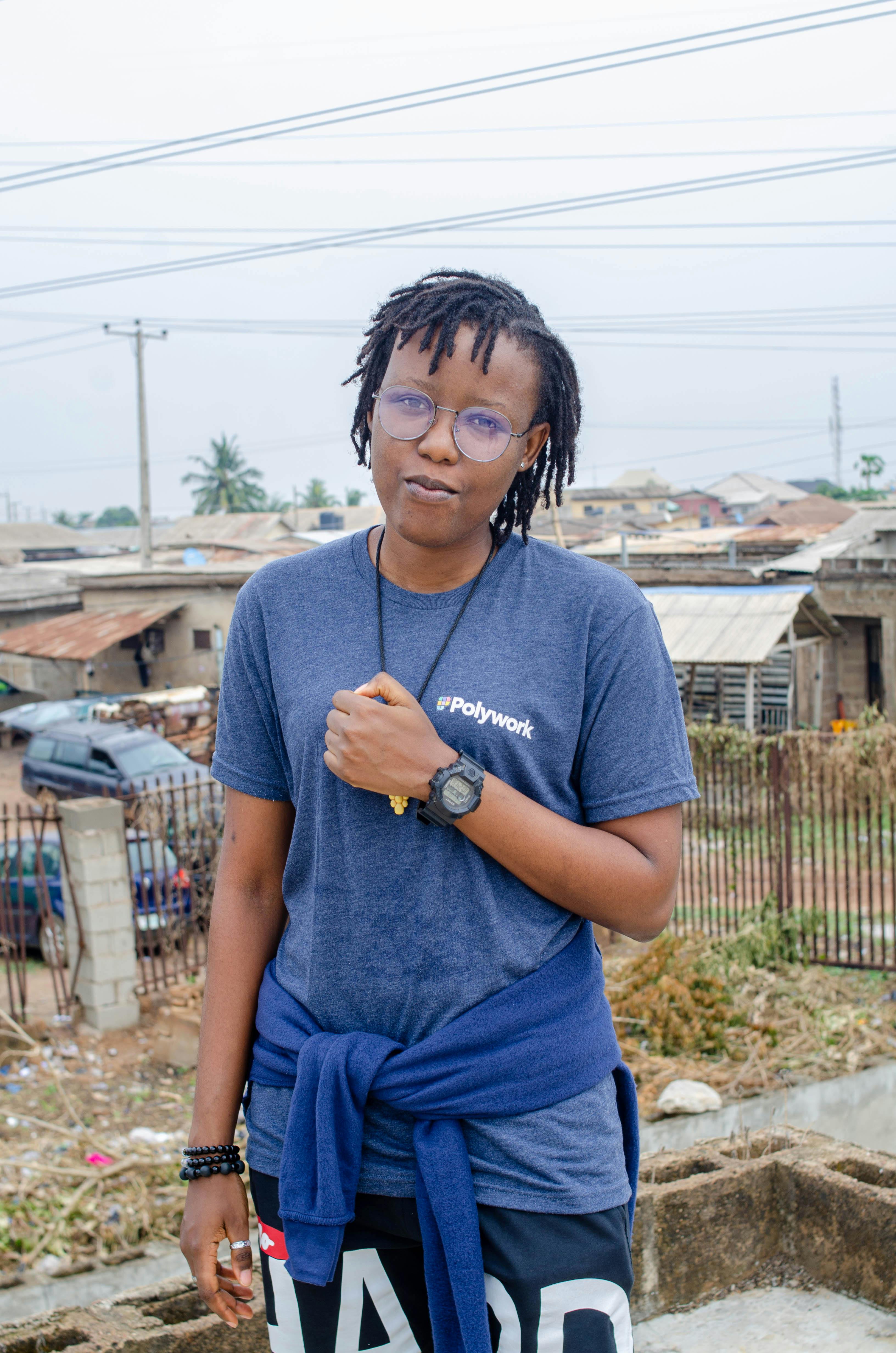 A stylish young person with glasses standing outside in an urban neighborhood.