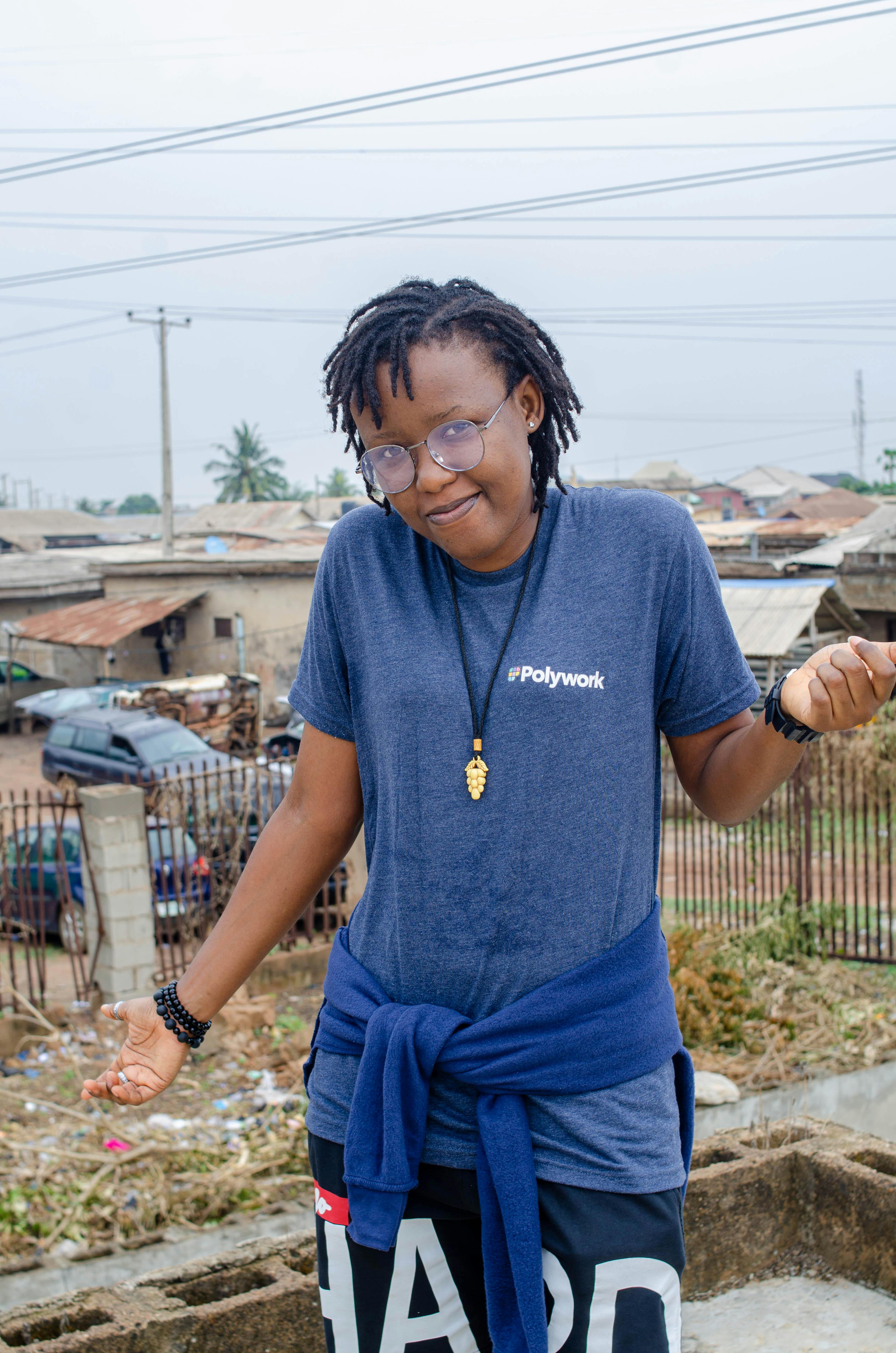 Woman in casual wear with eyeglasses standing outdoors in a village setting.