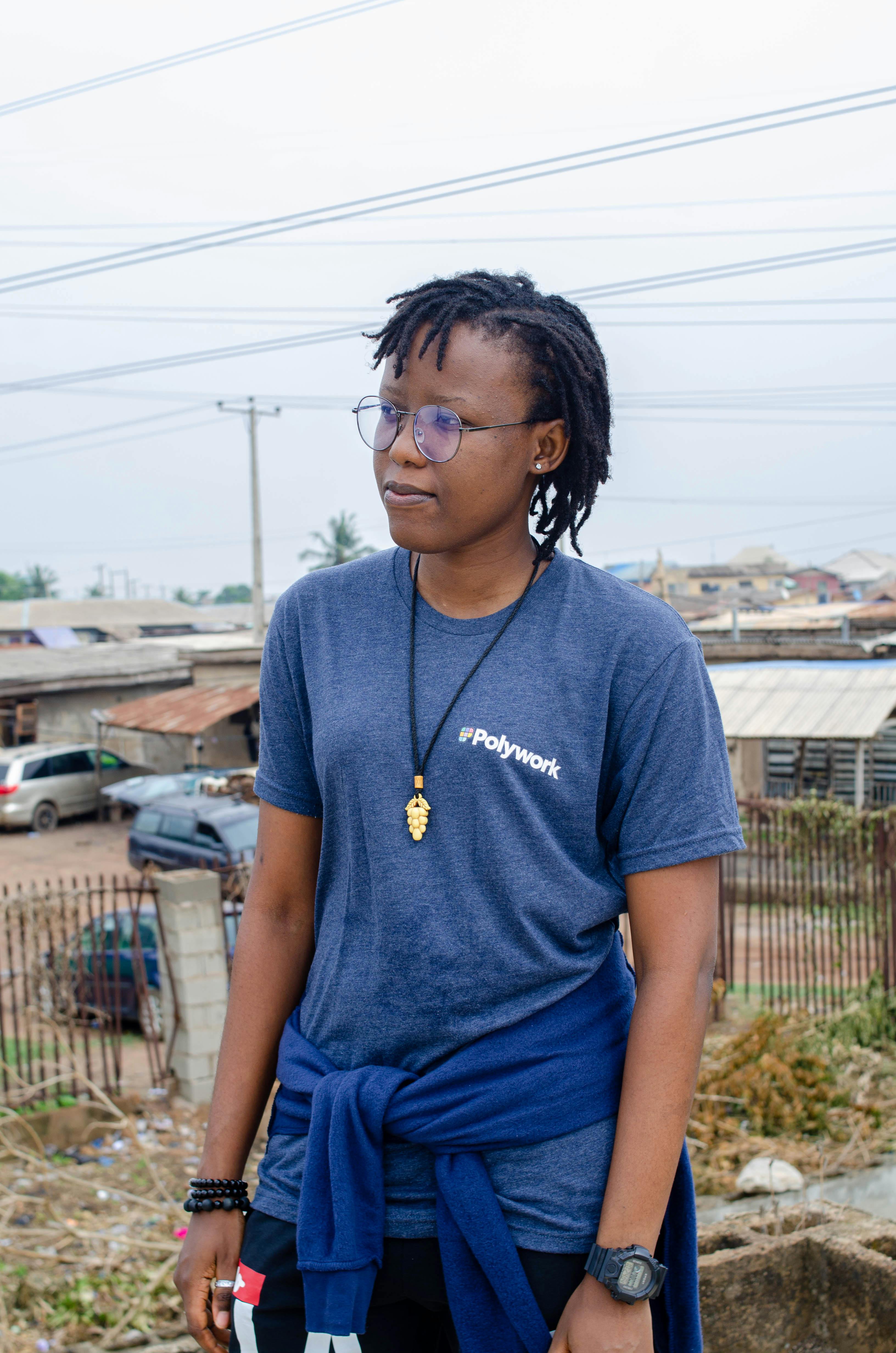 A woman wearing a casual outfit stands outdoors in an urban setting, showcasing modern fashion.