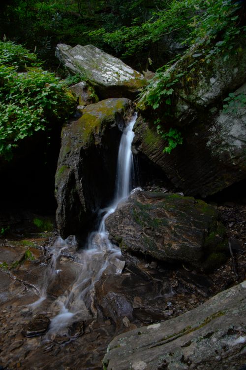 Free A peaceful waterfall cascades over moss-covered rocks in a lush forest setting, offering a tranquil nature scene. Stock Photo