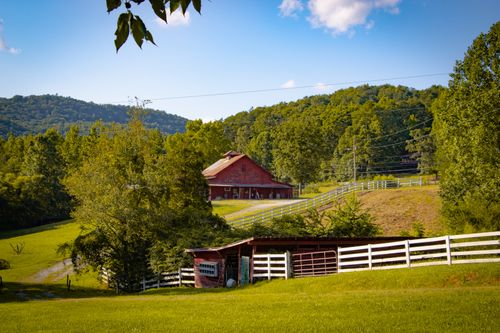 Free Tranquil rural scene featuring a classic red barn amidst lush green hills. Stock Photo