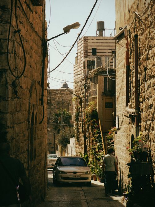 Free Romantic view of a narrow street in a historic old town with a parked car and pedestrians. Stock Photo