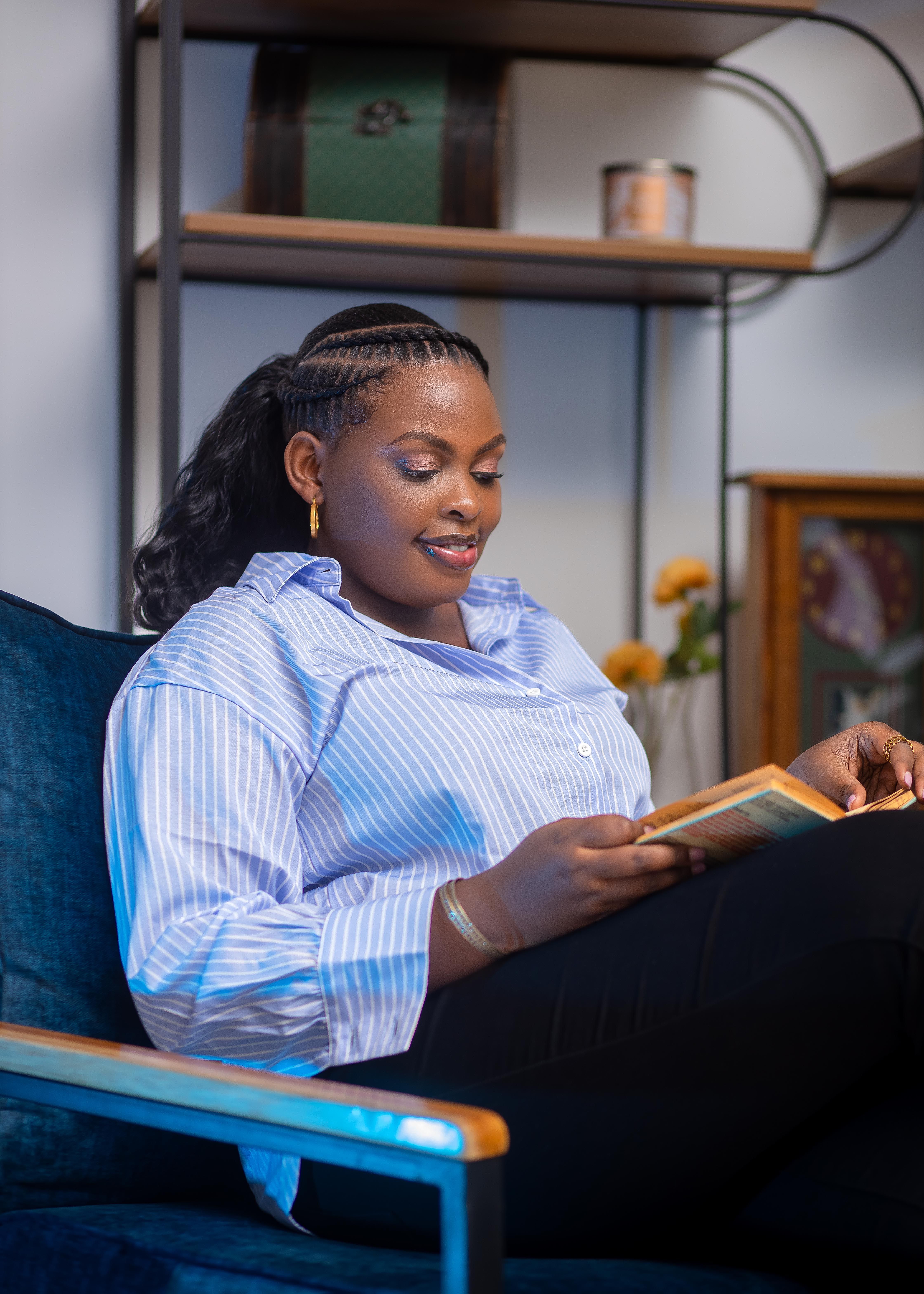 A young woman enjoys a moment of relaxation and reading indoors on a cozy chair.