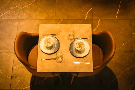 Top view of a modern restaurant table with plates, cutlery, and glasses set for two.