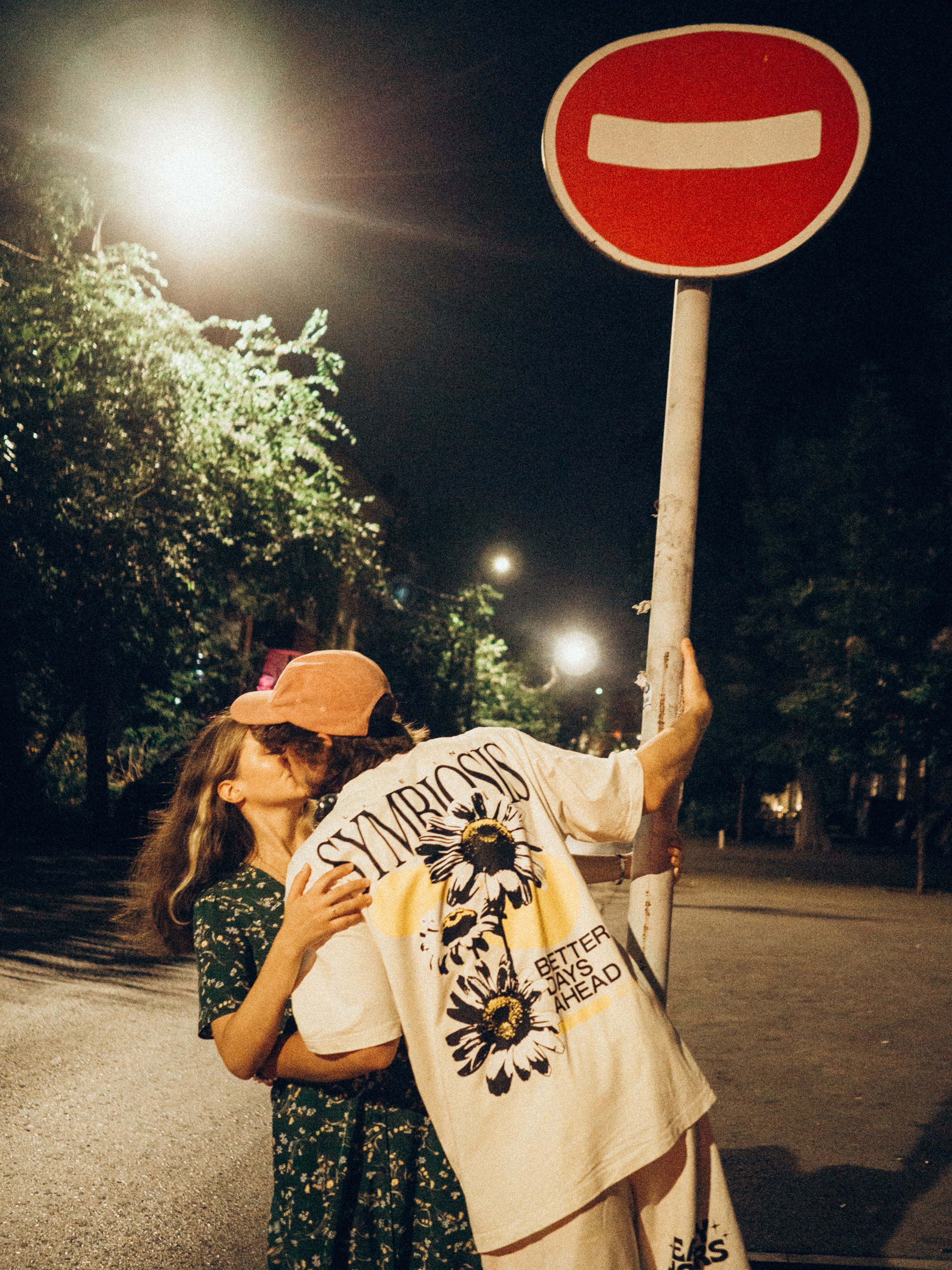 A couple sharing a kiss under a street sign in a city at night.