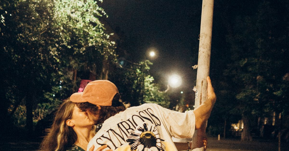 Rüyada Yasak Aşk Yaşamak - Rüya Tabiri ve Anlamı - A couple sharing a kiss under a street sign in a city at night.