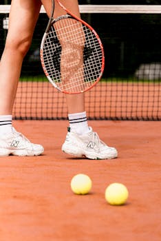 Close-up of a tennis player with racket and balls on clay court.