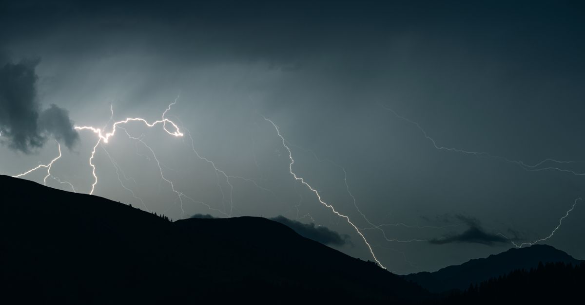 Captivating shot of lightning illuminating a dark sky over mountain silhouettes during a thunderstorm.