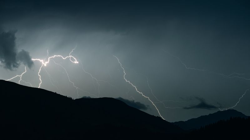 Captivating shot of lightning illuminating a dark sky over mountain silhouettes during a thunderstorm.