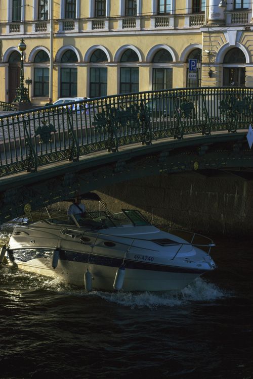 Free Motorboat navigates a canal under a historic bridge in a European city with vibrant architecture. Stock Photo