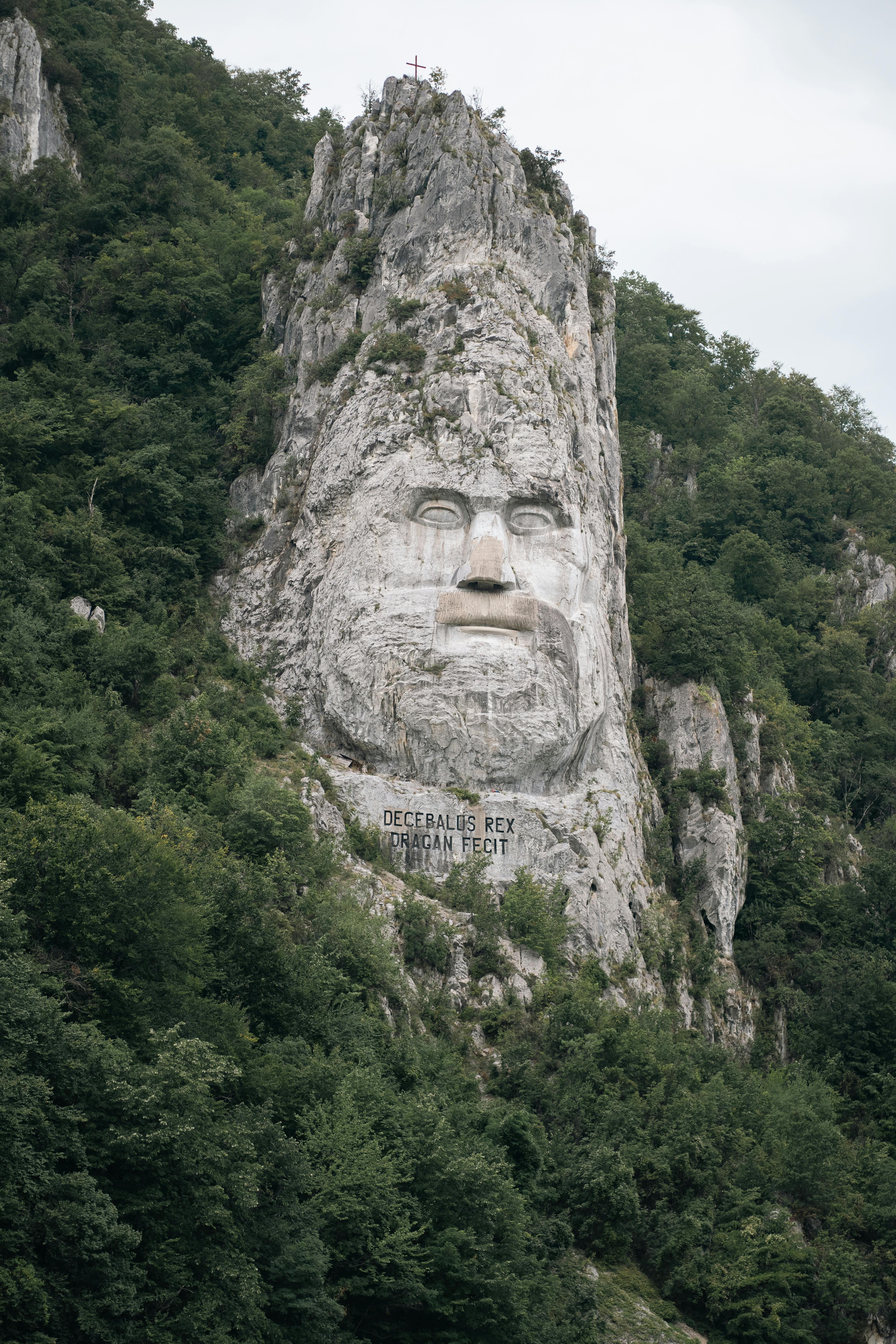 The monumental Decebalus rock sculpture in Romania, surrounded by lush forest.