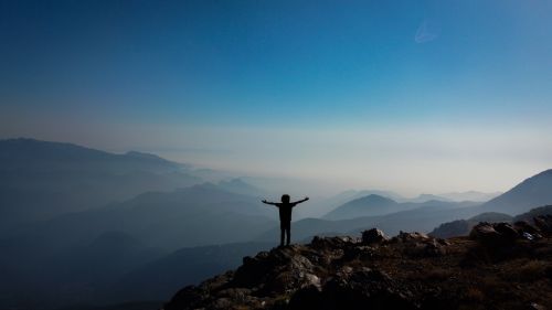Free Silhouette of a man standing with stretched arms on a mountain peak at sunrise, capturing the essence of freedom and adventure. Stock Photo