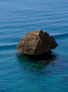 A single eroded rock sits serenely in calm, blue ocean waters. Captivating nature scene.