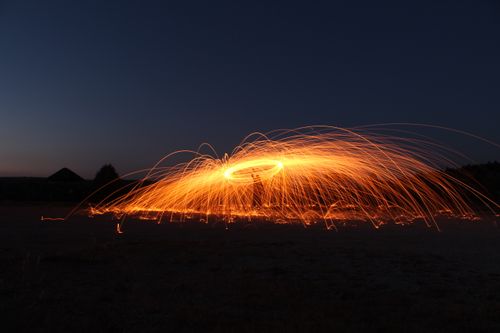 Free Dazzling light trails from a steel wool spin illuminate the night sky in a dynamic outdoor setting. Stock Photo