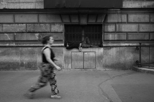 Free A black and white street photography scene showing a woman walking past a man resting on a city sidewalk. Stock Photo