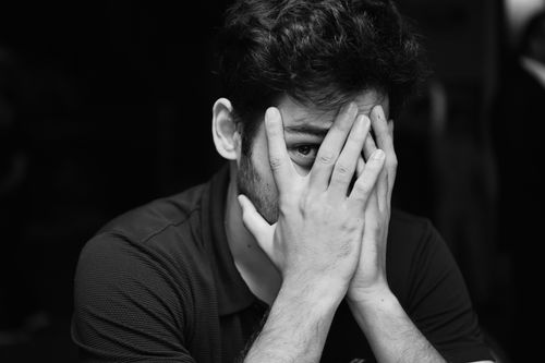 Free Black and white portrait of a young man with hands covering face in studio. Stock Photo